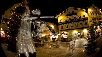 Geigenspieler-Statue vor Adventmarkt in St. Gilgen bei Nacht